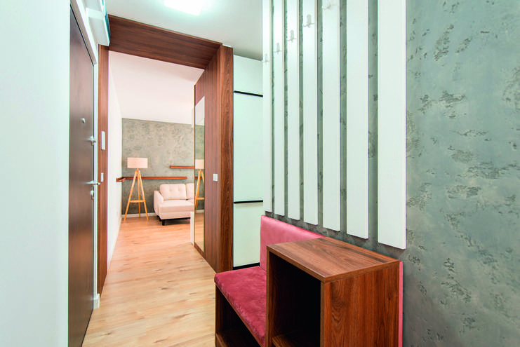 Modernes Entrée mit Holzverkleidung, einer roten Bank und Blick auf einen hellen Wohnraum mit Sofa und Stehlampe.