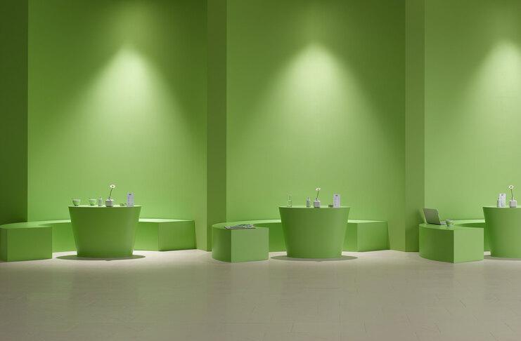 Grüne Einrichtung als Ladenimpressionen mit Sitzmöglichkeiten und indirekter Wandbeleuchtung.